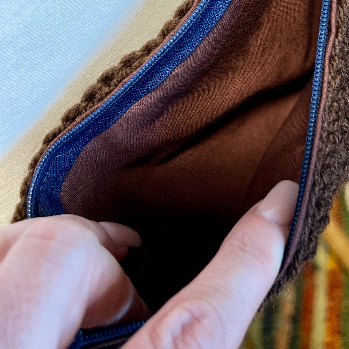 Close-up of a hand holding a brown fabric item with blue stitching.